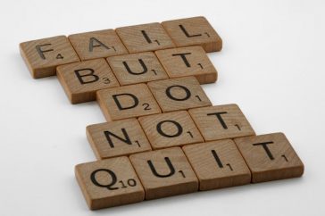 Close-up of Scrabble tiles forming the motivational phrase 'Fail but do not quit' on a white surface.