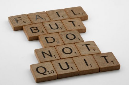 Close-up of Scrabble tiles forming the motivational phrase 'Fail but do not quit' on a white surface.
