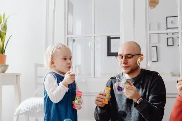 A joyful moment between a father and daughter blowing bubbles indoors, highlighting family fun.